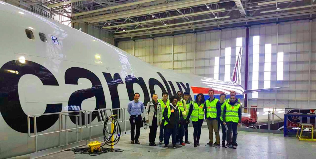 A group of 11 students next to a Cargolux plane. Seen of the students are wearing bright green safety vests