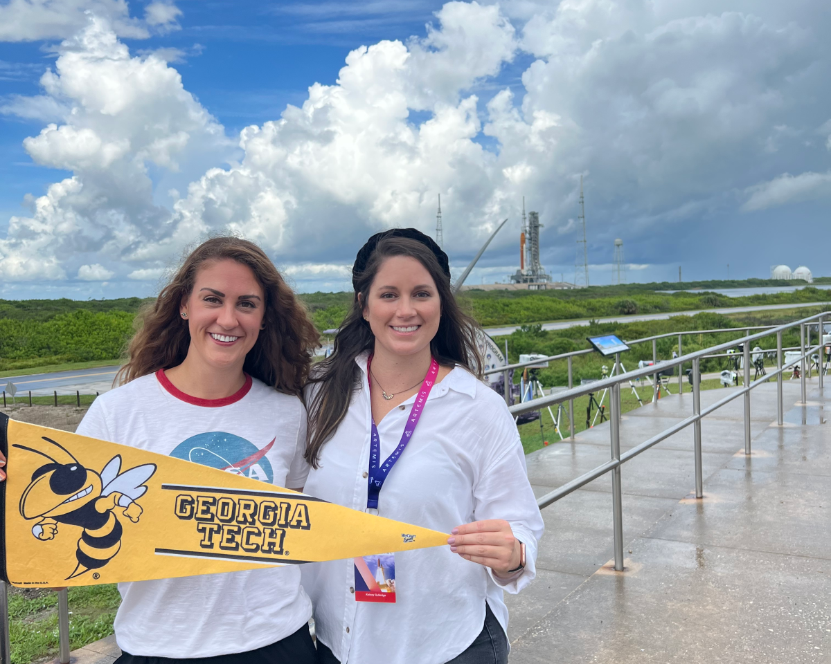 Kate Gunderson and Kelsey Gulledge stand with a Georgia Tech flag as Artemis I proudly stands in the background